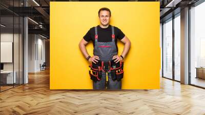 Portrait of happy handyman with tools belt isolated on yellow background Wall mural